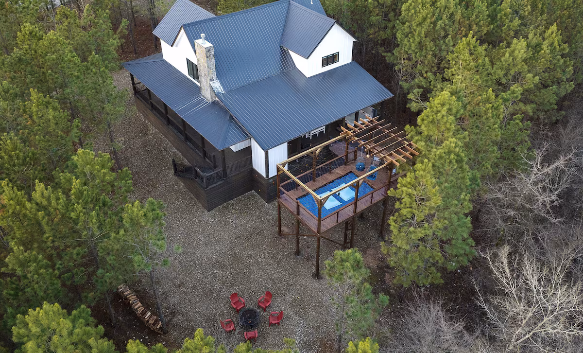 Aerial view of the cabin, net deck, and fire pit among the pines